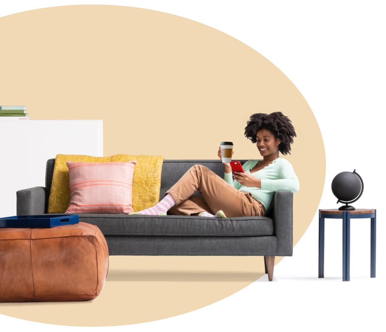 一个女人坐在沙发上，端着咖啡，一边用iPhone看租房pp王者电子官网的内容. A globe sits on side table.